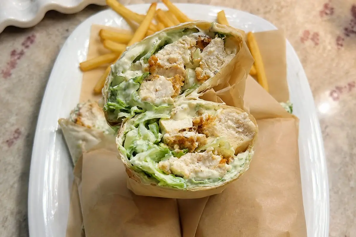 Crispy chicken wrap cut in half showing crispy chicken, romaine and creamy dressing, served with fries