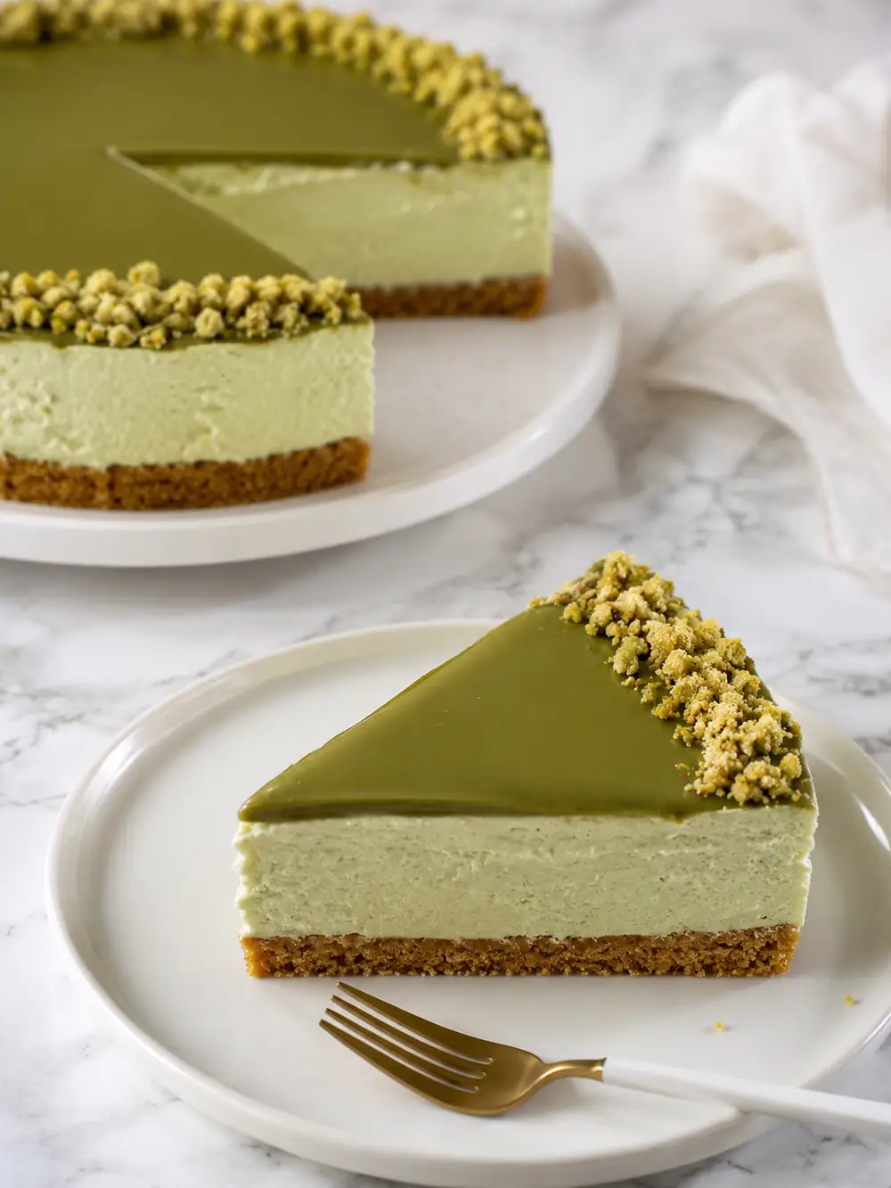 Whole no bake pistachio cheesecake with a glossy green pistachio top layer and one slice being lifted out