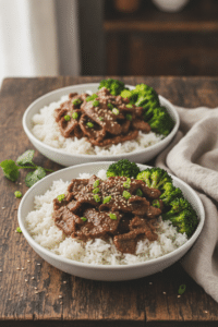 Garlic ginger beef rice bowls served in shallow white bowls over steamed rice, glossy sliced beef and bright broccoli on top